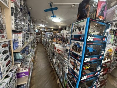 模型店内の通路。棚や床にプラモデルやラジコンの箱が大量に積み上げられている。