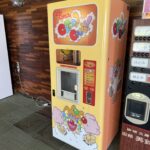 木目調の壁の前に置かれた、ピエロのイラストが描かれた黄色のレトロな綿あめ自動販売機。